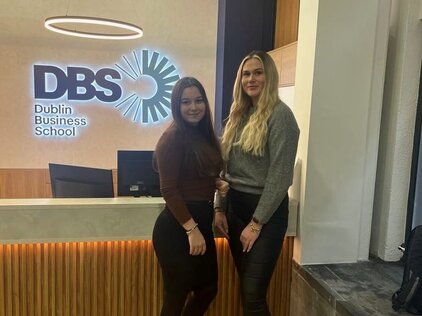Foto von zwei jungen Frauen, die vor dem Schild der Dublin Business School stehen. 
