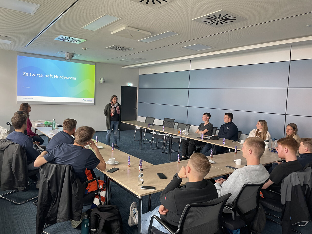 Eine Gruppe von Personen, die an einer U-förmigen Tafel sitzen und sich eine Präsentation anschauen. 