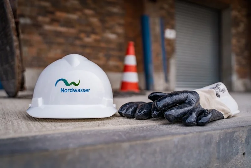 Weißer Bauhelm mit Nordwasser-Logo und Arbeitshandschuhe