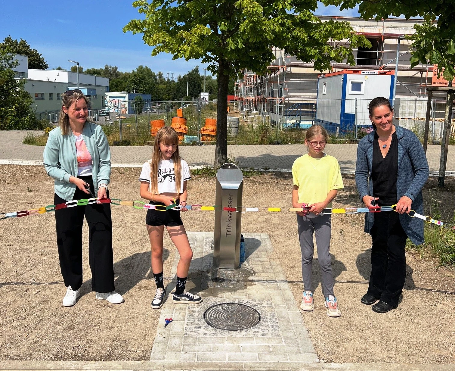 Zwei Frauen und zwei Kinder stehen vor dem neuen Trinkbrunnen und schneiden gemeinsam symbolisch das Band durch