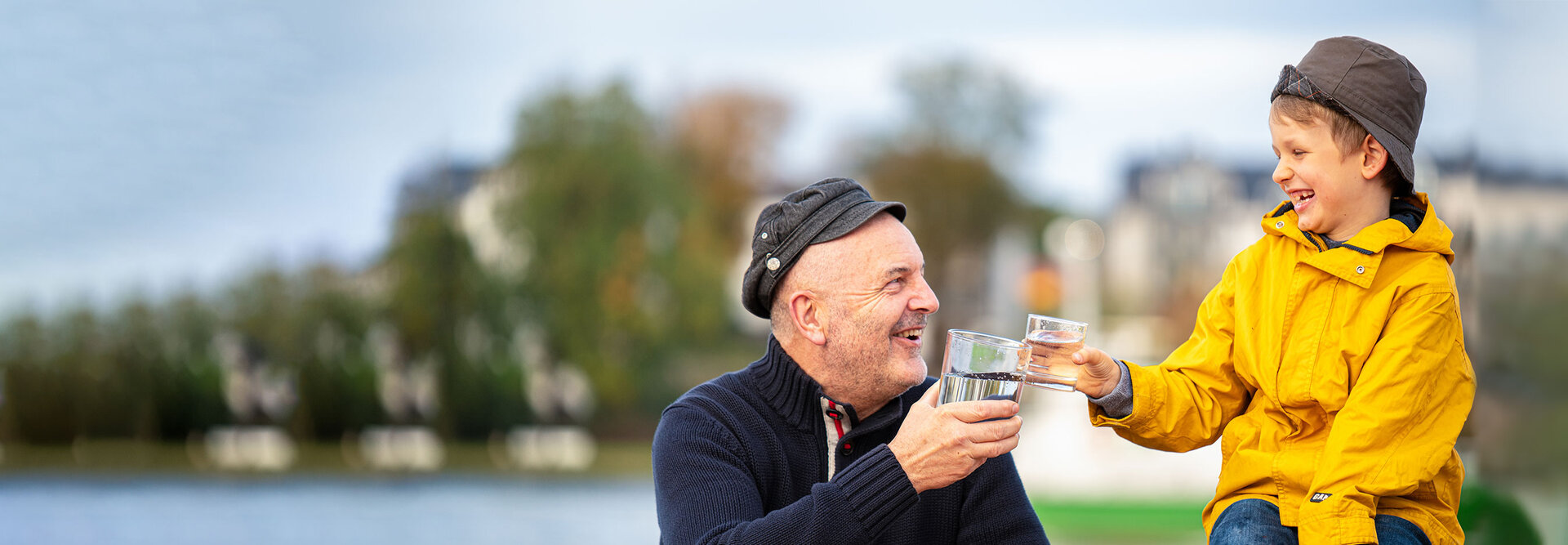 Ein älterer Mann und ein Junge sitzen im Freien und stoßen mit einem Glas Wasser an.