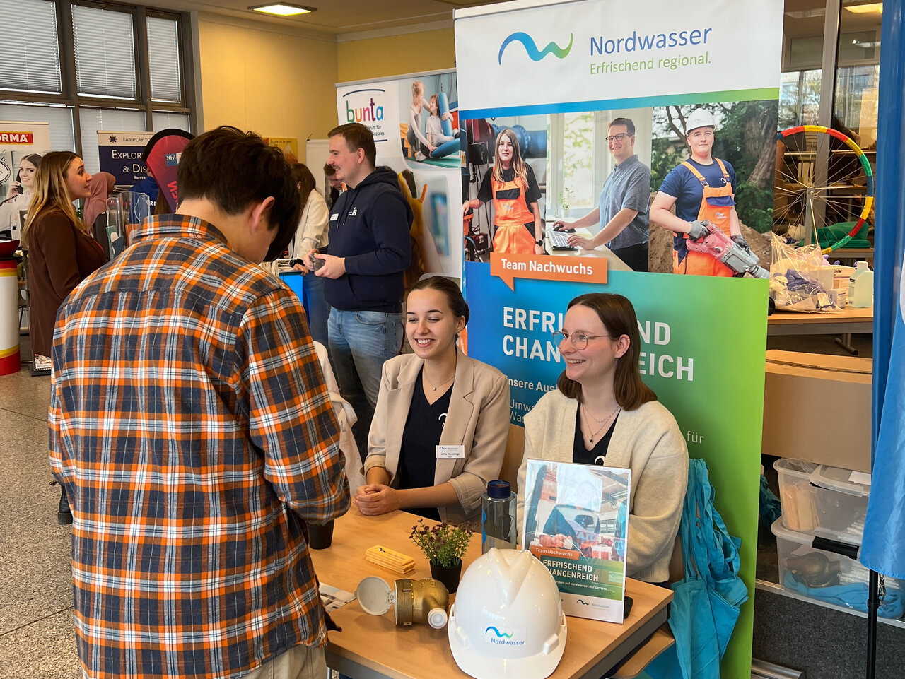 Ein Schüler steht vor einem Tisch an dem zwei Mitarbeiterinnen von Nordwasser sitzen