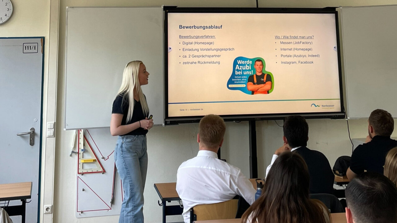 Foto einer Frau, die neben einem Bildschirm steht und eine Präsentation hält. 