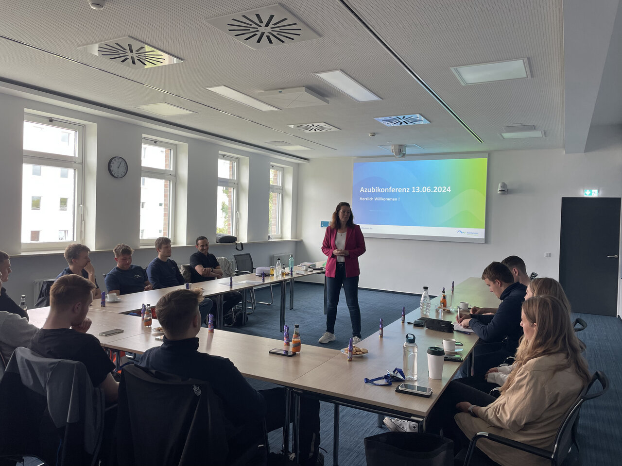 Eine Gruppe von Personen, die an einer U-förmigen Tafel sitzen und sich eine Präsentation anschauen. 