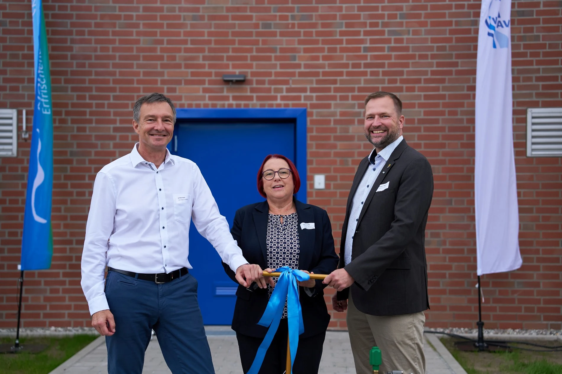 Drei Personen, darunter eine Frau, stehen vor dem neuen Speicherbauwerk und drehen gemeinsam an einem Schieberschlüssel